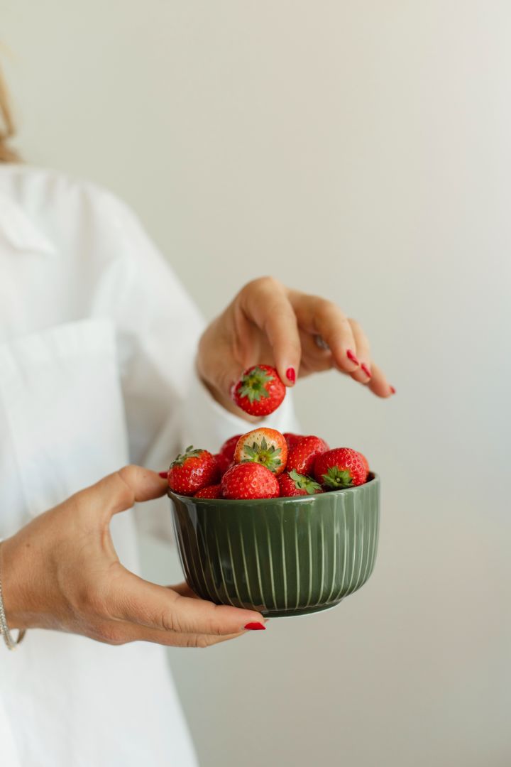 Ebba Kleberg von Sydow håller i tidlösa designklassikern Hammershøis mörkgröna skål från Kähler som är fylld med jordgubbar.