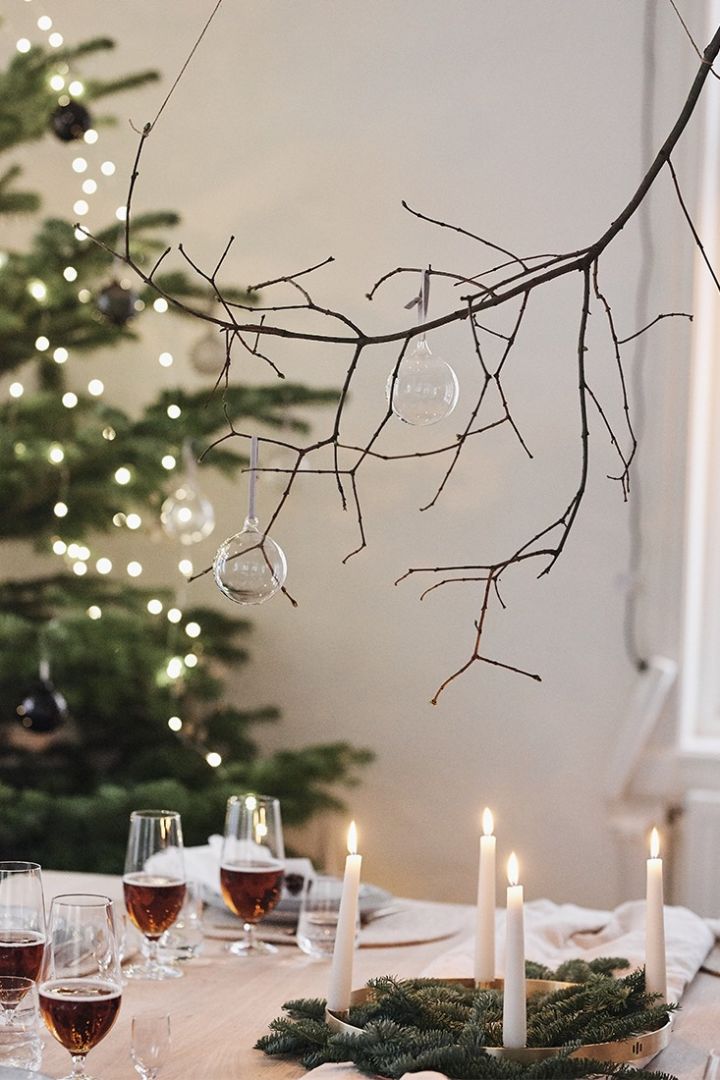 En gren hänger över en vit, naturinspirerad juldukning iklädd julgranskulor från Iittala som en inspirerade centerpiece. 