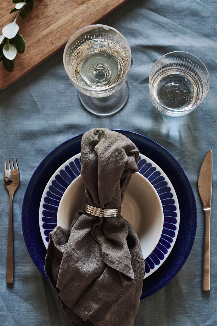 Ett blåvitt tallrikskuvert välkomnar gäster till bords med sin kornblå nyans och tallrik från Iittala, Götefors porslin och Nordic Nest. 