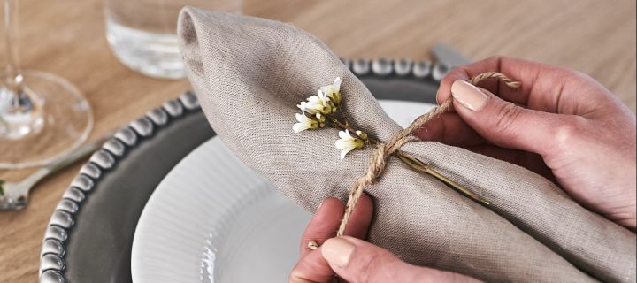 Beige linneservett från Scandi Living i enkel servettvikning med jutesnöre och blomma.