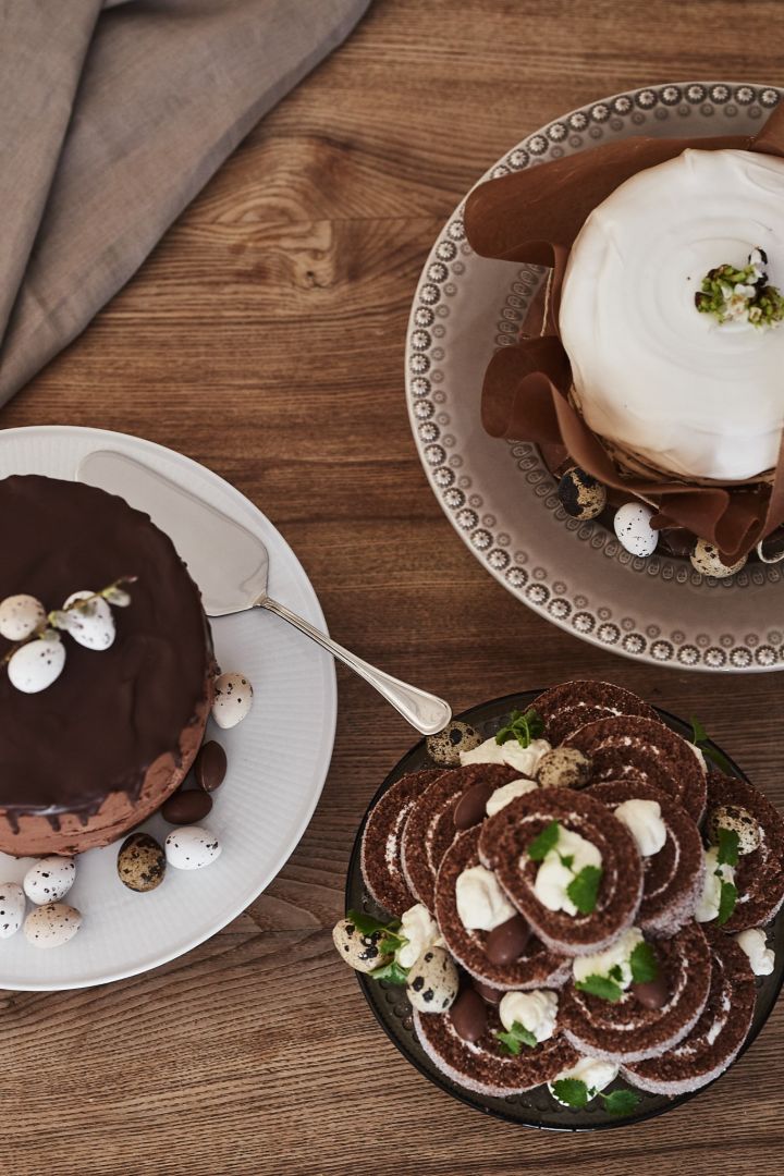 Tre tårtor står serverade på påskdukningen som årets påskdessert: en chokladtårta, morotstårta och rulltårta.
